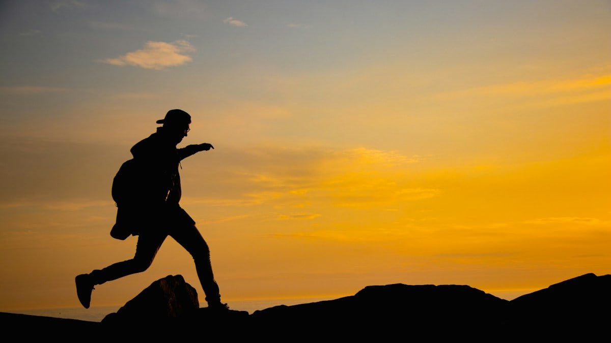 A silhouette of a person running on a hill at sunset